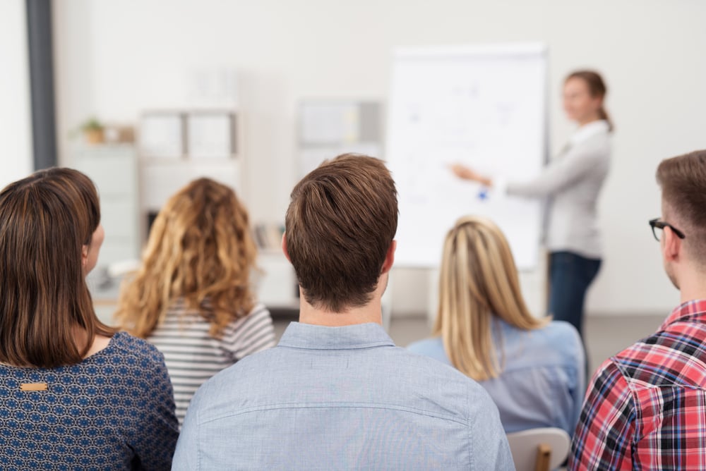 Rear View of Young Office Workers in Casual Outfits Listening to a Top Manager Explaining Something Using Illustrations. Rear View of Young Office Workers in Casual Outfits Listening to a Top Manager Explaining Something Using Illustrations.